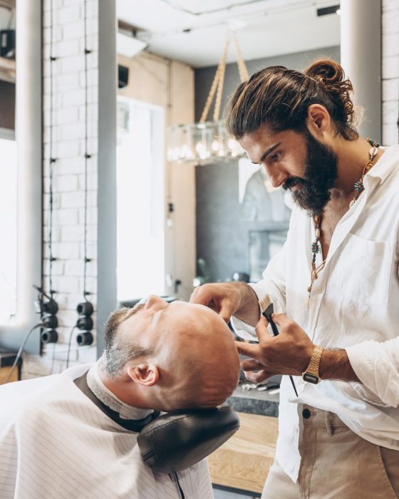 making hairstyle for man in a Barber shop, Latin American man gives a haircut to a bald bearded man